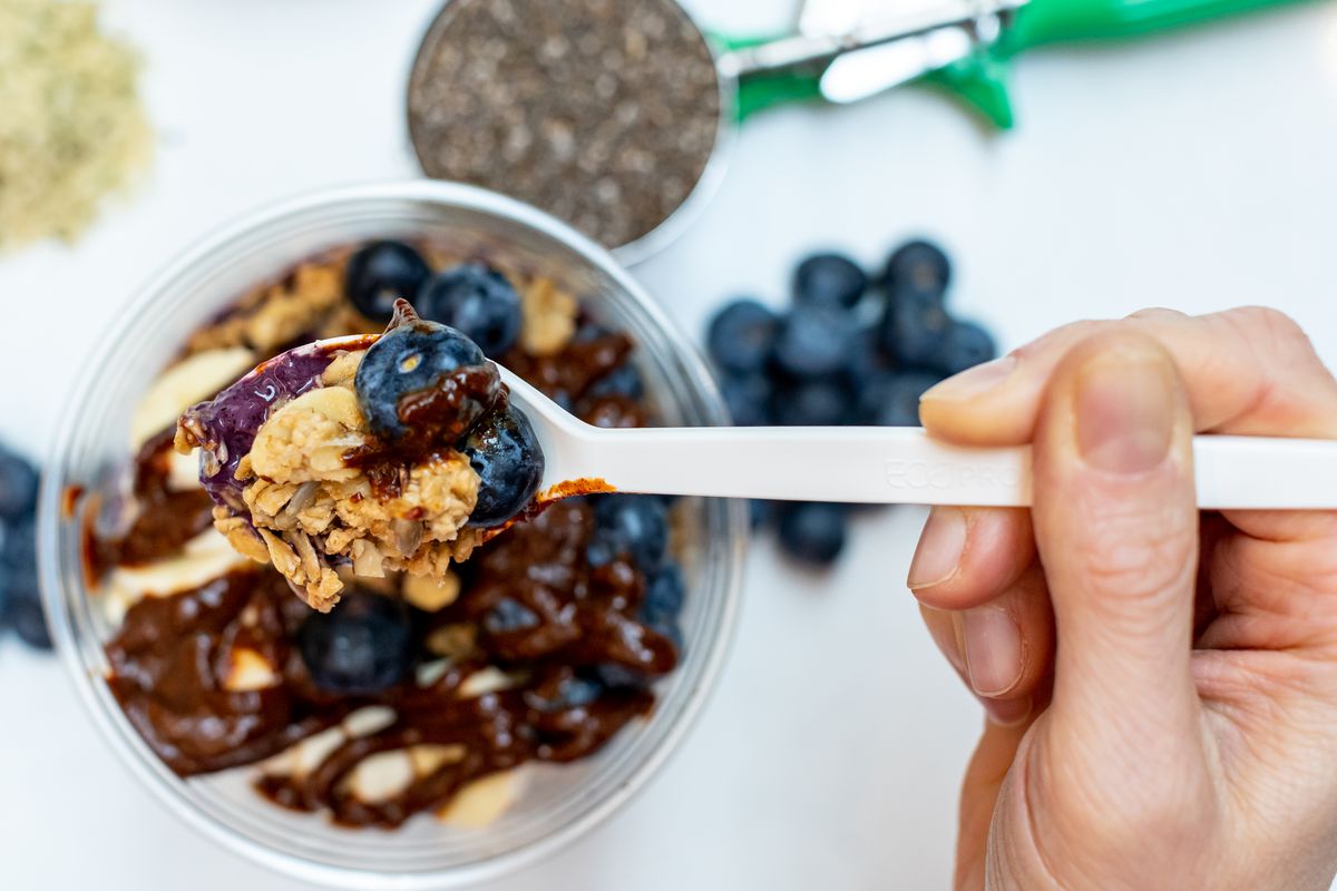 A spoon going into a smoothie bowl filled with blueberries.
