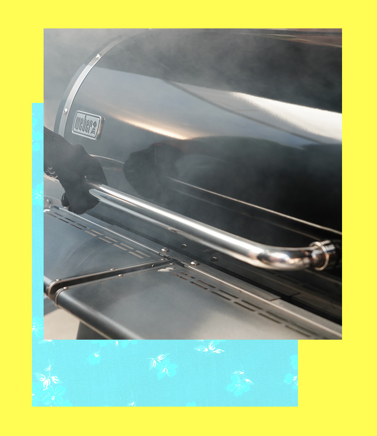 A gloved hand holds the front bar of a Weber grill. 