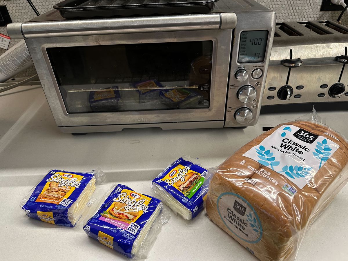 Three packages of Kraft flavored singles and a loaf of bread in front of a toaster oven