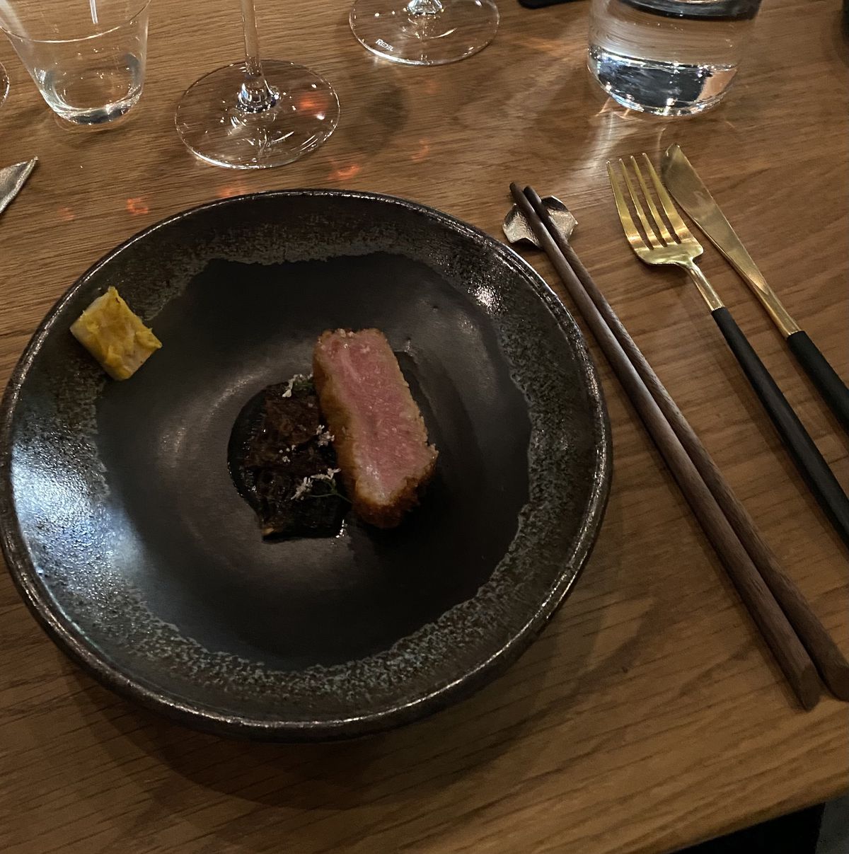 A piece of A5 wagyu beef with a black pool of curry and local morel mushrooms.