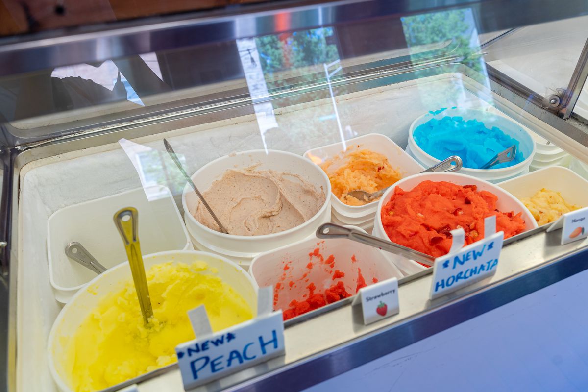 An ice cream cooler filled with buckets of Italian ice in different colors.