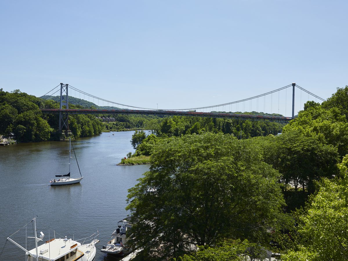 A body of water surrounded by trees. There is a bridge in the distance and a boat in the water.