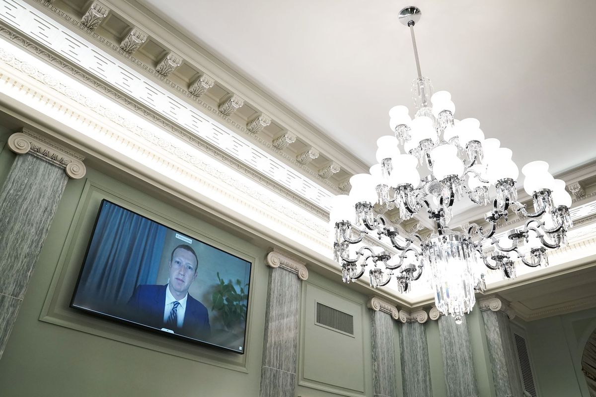 Facebook CEO Mark Zuckerberg appears on a screen on the wall of the Senate beside a large chandelier.