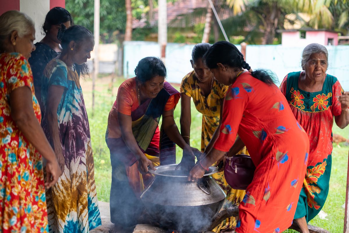 Women gather around a large pot cooking outside.