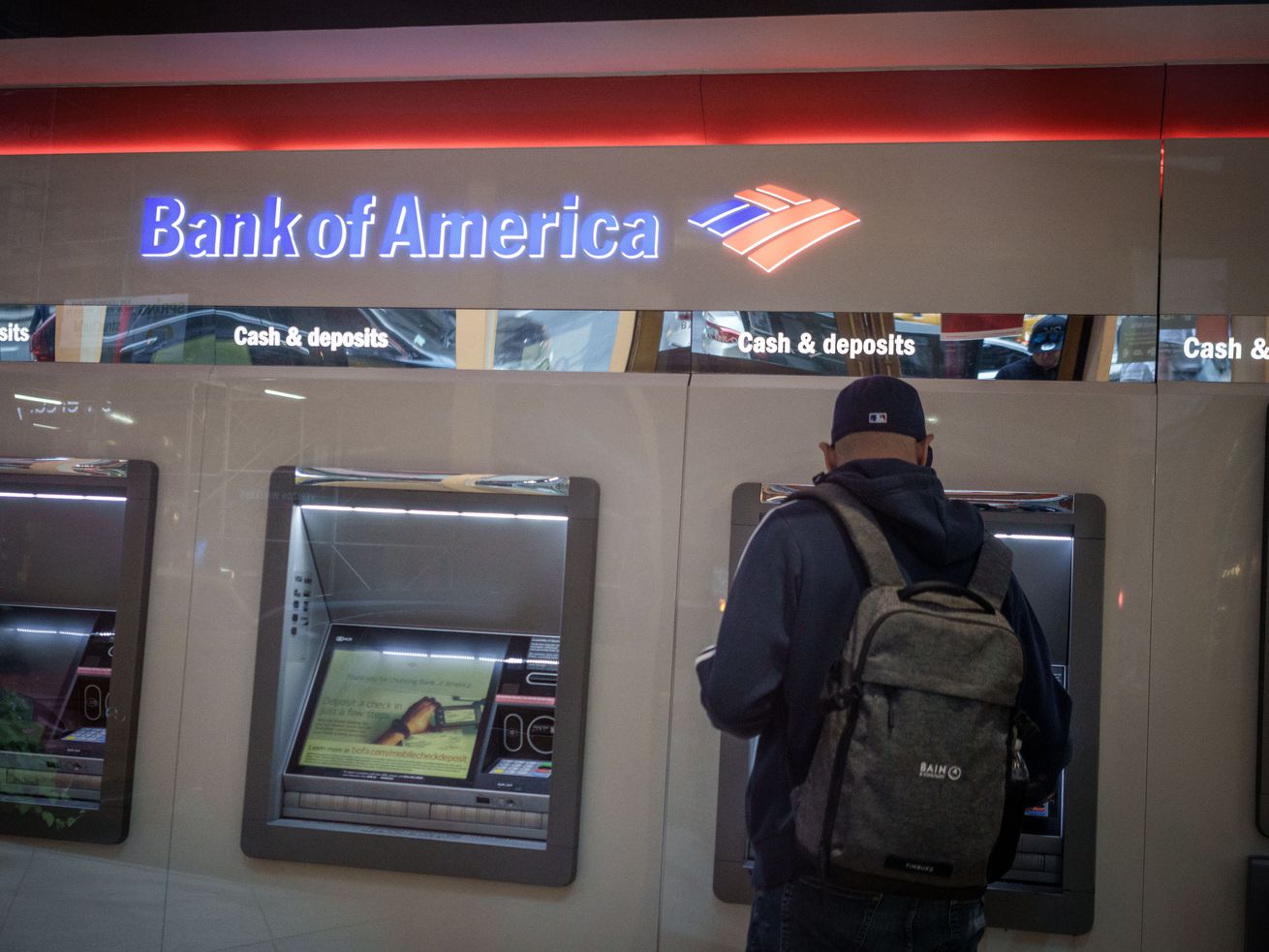 A person carrying a backpack stands at a Bank of America ATM.