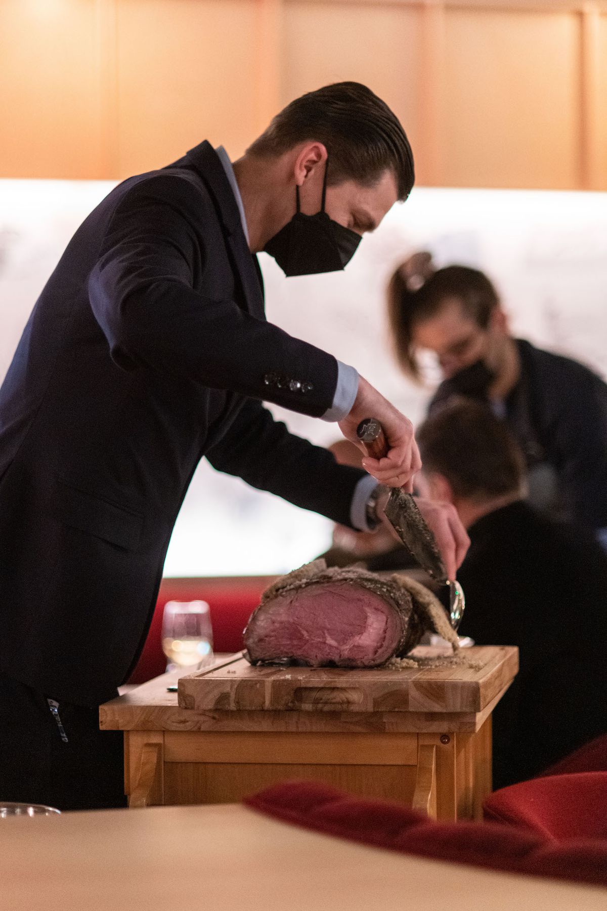 A server cuts prime rib from a full rack at a dining room tableside preparation.