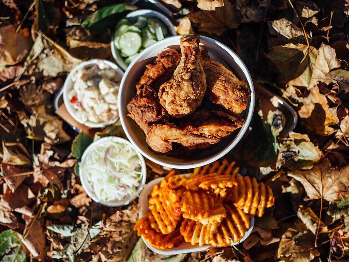 A bucket of fried chicken from Bucktown Chicken &amp; Fish sits on the ground, which is covered with fallen leaves. There are also waffle fries and other sides.