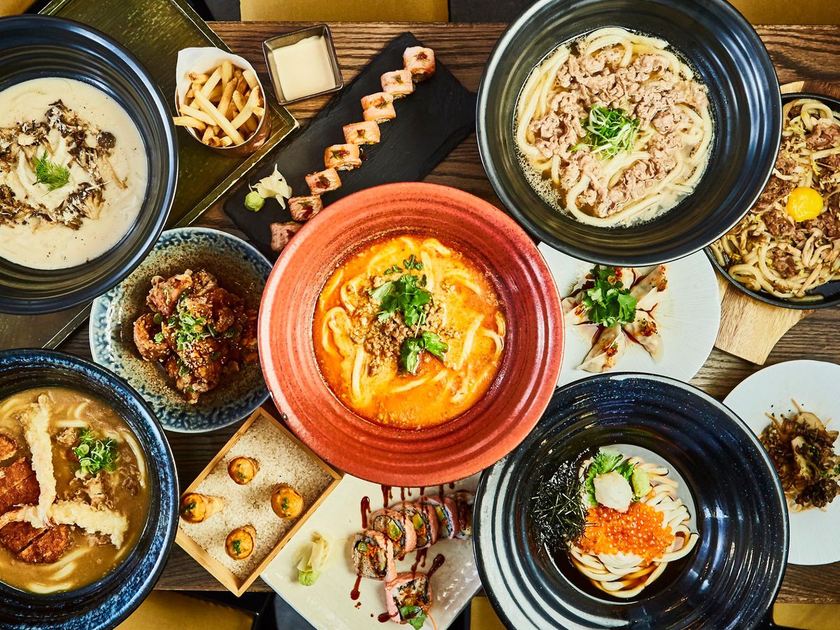 A table full of dishes, including multiple noodle soups, maki rolls, gyoza, and uni appetizers