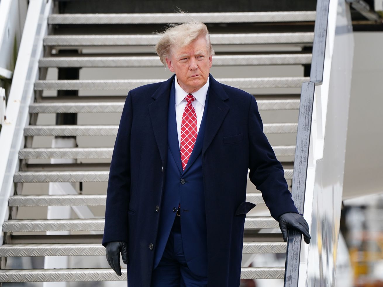 Donald Trump descending an airplane stairway with his hair blown askew.