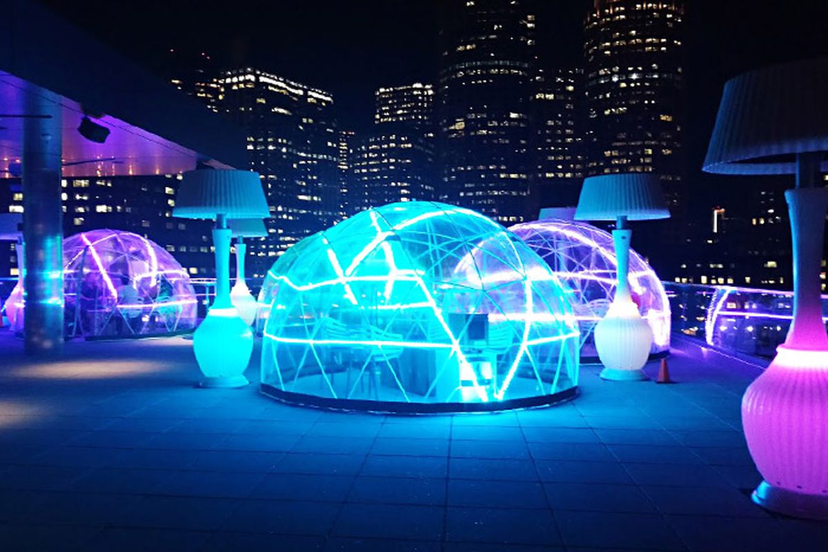 Glowing see-through igloos sit on a rooftop with city skyline views in the background.