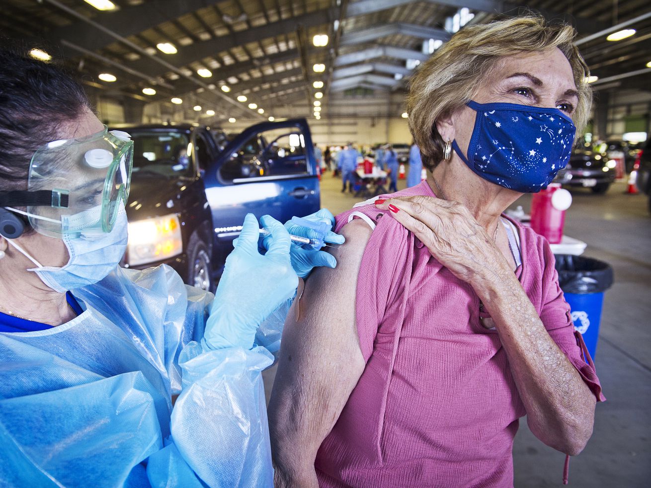 A health care worker giving a masked person a shot in the arm.
