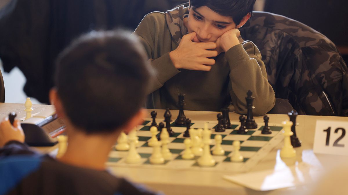 Two tweens sit opposite each other playing a game of chess.