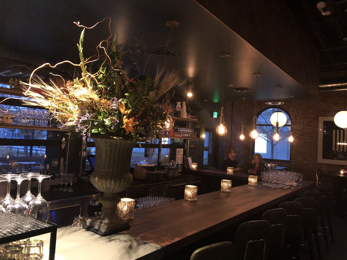 A photo of the bar at Postino and a large plant in a vase on top of it 