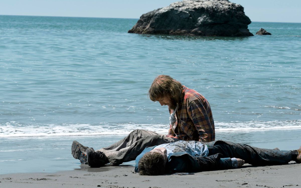 On a deserted beach, Hank (Dano) sits next to a corpse (Radcliffe).