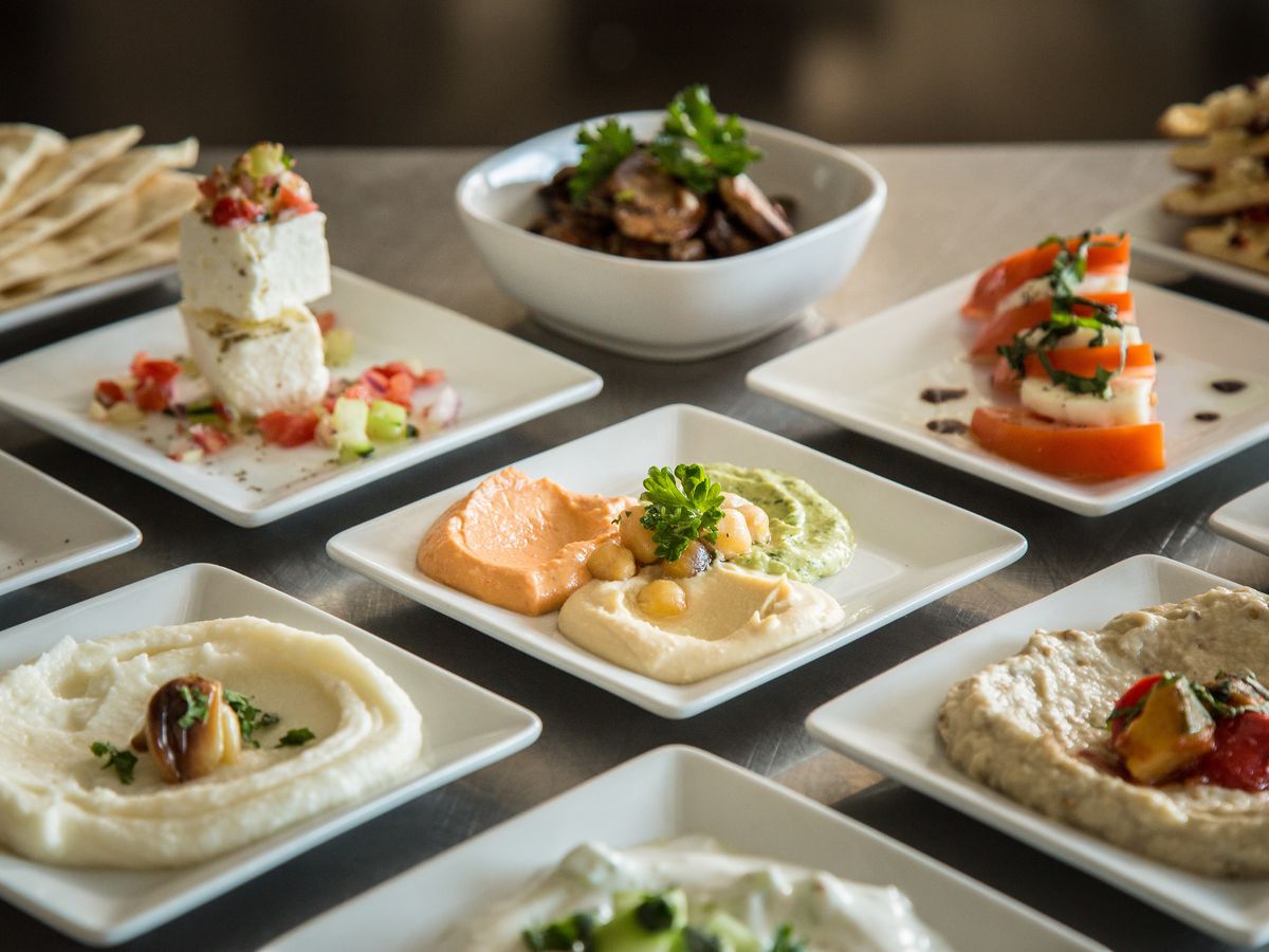 Square white plates featuring various dips and caprese salad on a table. 