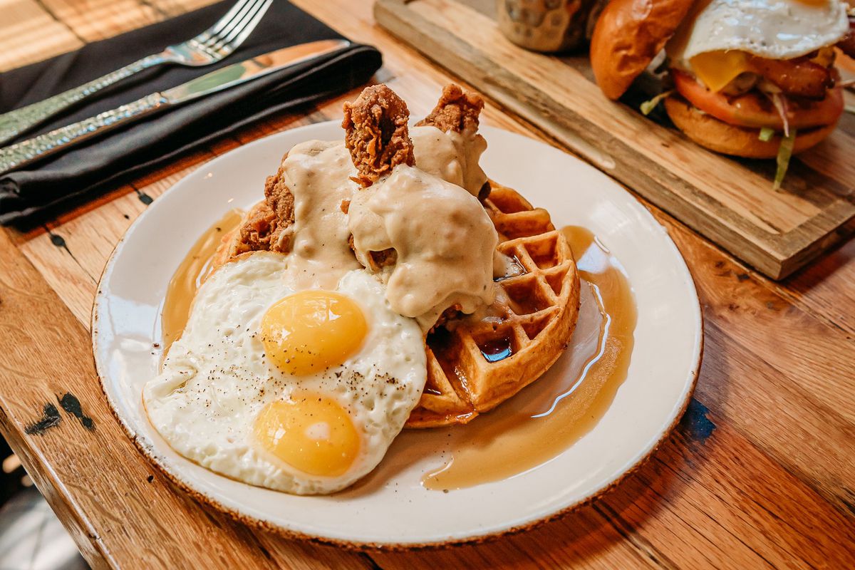 A Belgian waffle topped with two sunnyside-up eggs and smothered fried chicken with maple syrup, from Haywire.
