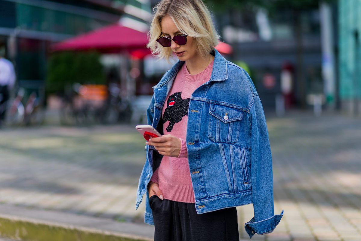 Fashion blogger Lisa Hahnbueck on her phone wearing a pink shirt and denim jacket
