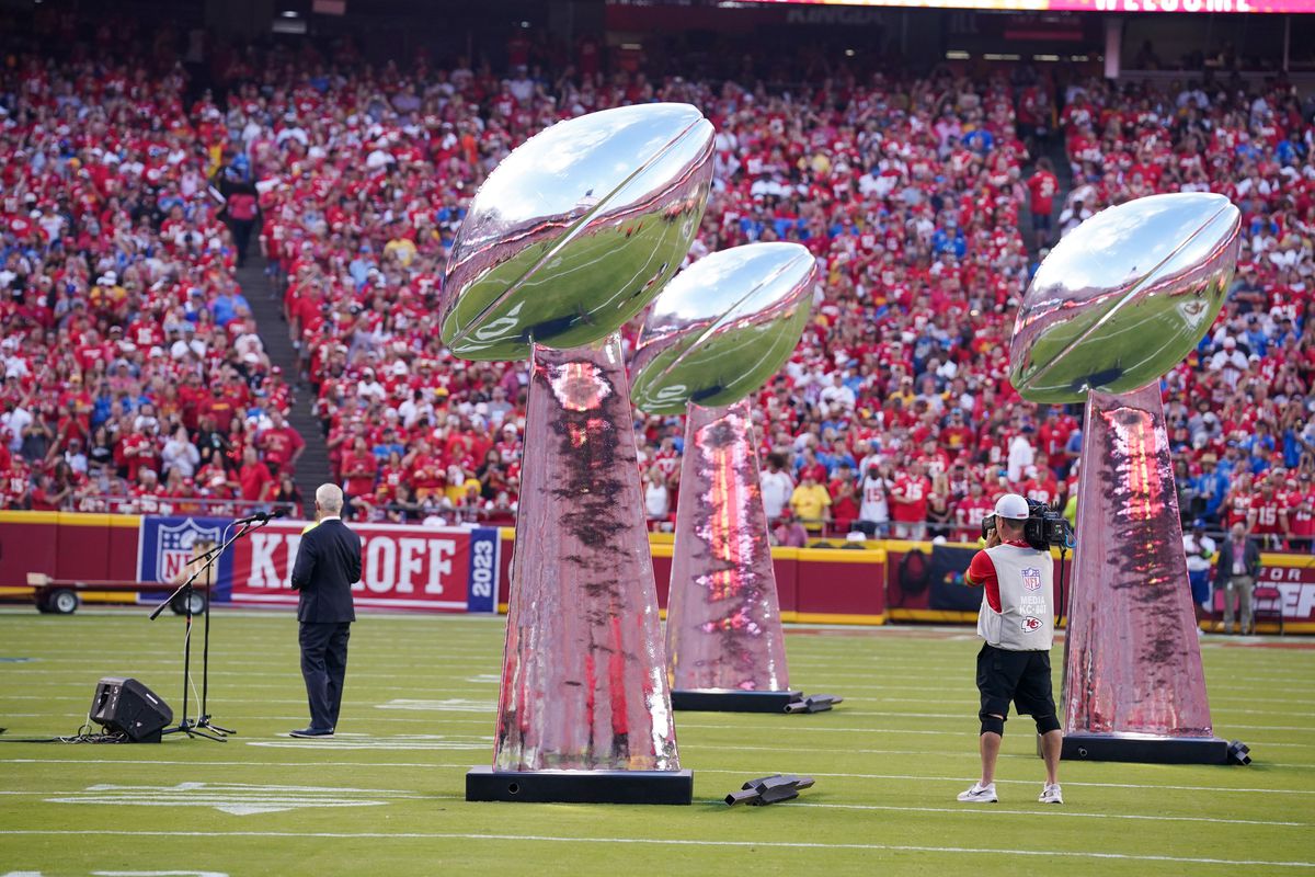 Three large replicas of the Vince Lombardi trophy stand on a football field