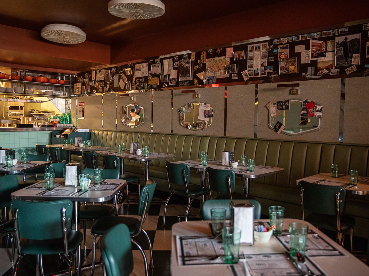 Pale antique green upholstered booths line the walls next to the kitchen at Karl’s. The walls feature vintage light fixtures, beige linoleum, and dark wood peg board covered in family photos and momentos.