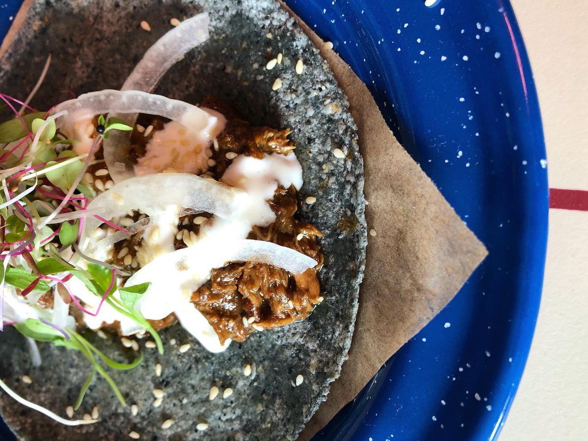 A taco on dark tortilla on a blue plate.