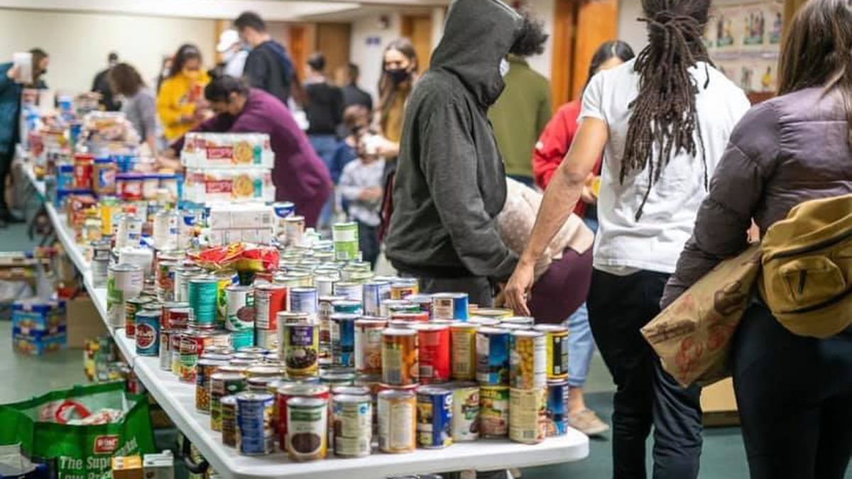 Volunteers stand around a table laden with canned goods, personal care supplies, and other donations 