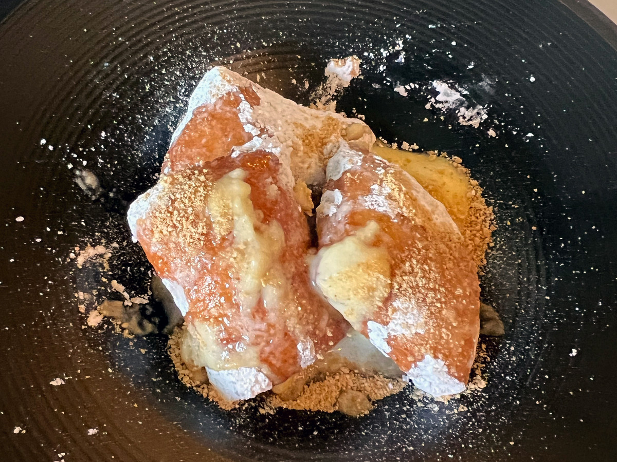 Three beignets covered in powdered sugar and leaking custard.