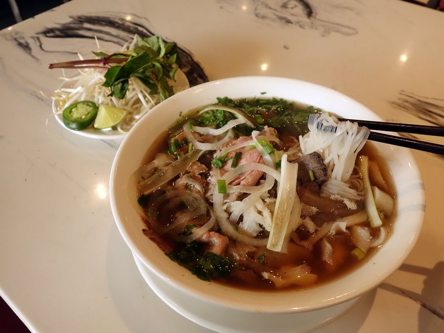 A bowl of pho with thin rice noodles, a variety of meat, and sliced onions and scallions.