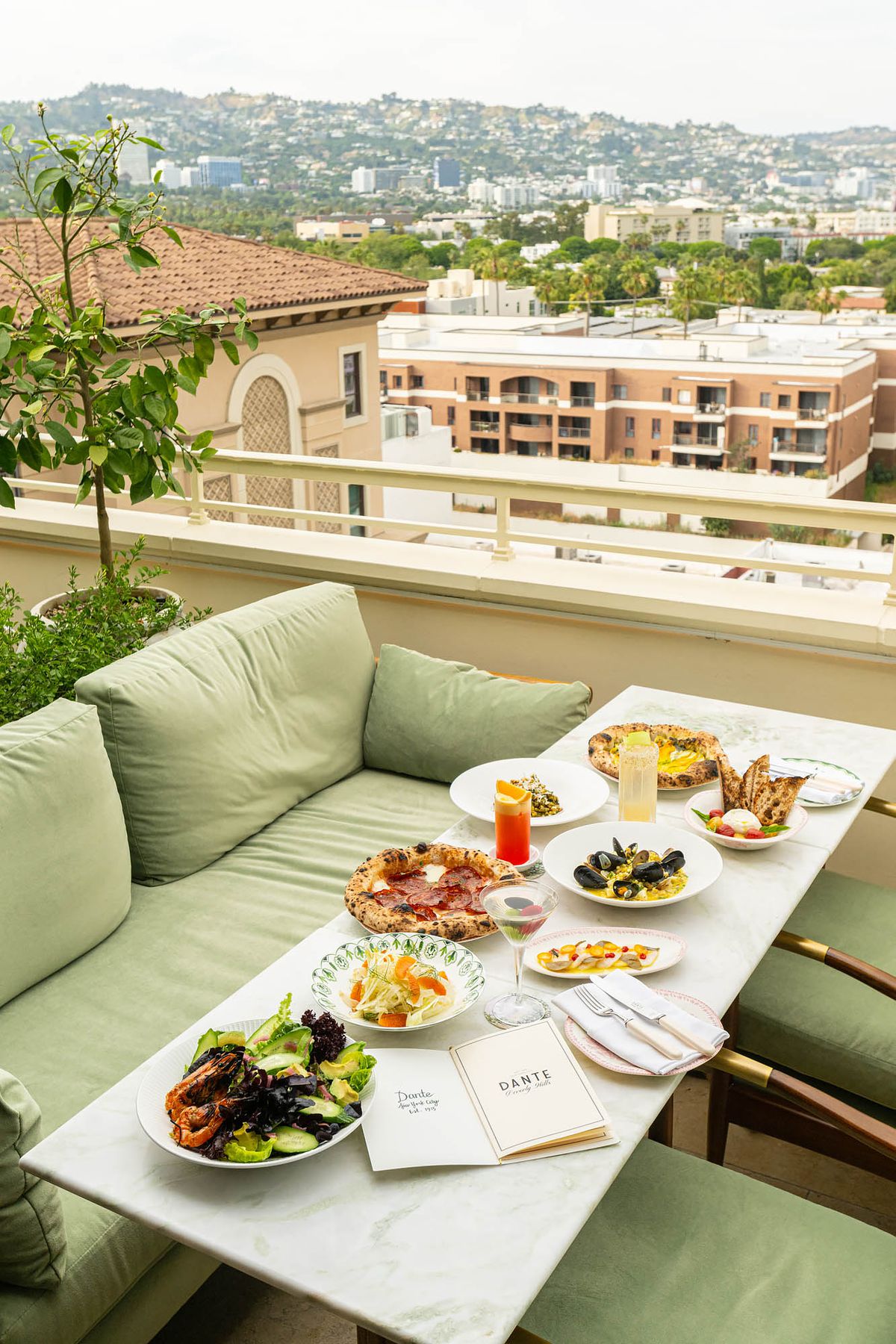 A green couch and white table filled with dishes on the patio at Dante Beverly Hills.
