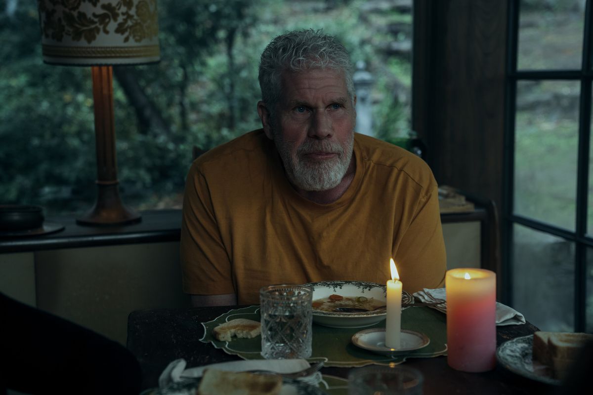 Ron Perlman looks sad in a yellow T-shirt at a candlelit dinner table at twilight in Mr. &amp; Mrs. Smith