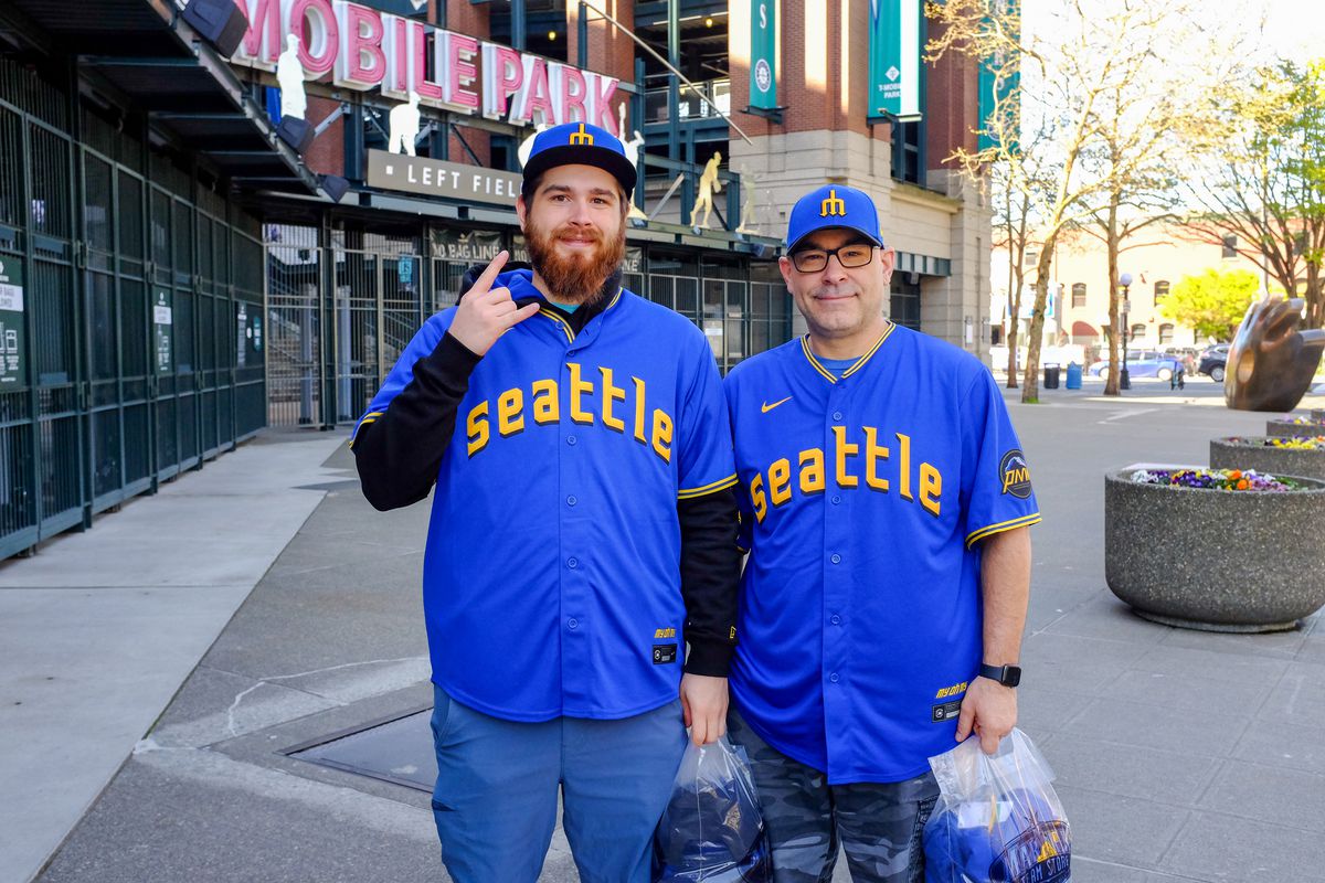 Two Mariners fans pose in their new City Connect jerseys outside the gates to T-Mobile Park