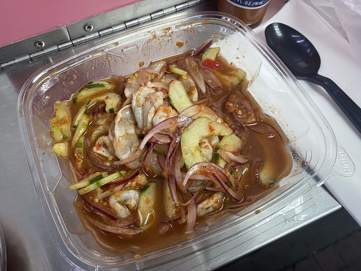 Red juices, red onion, cucumber, and pieces of seafood slosh around in a plastic container.
