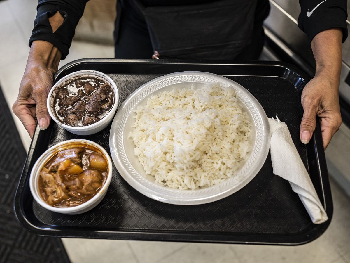 A person holding a black tray of with a large plate of rice and two sides in foam bowls.