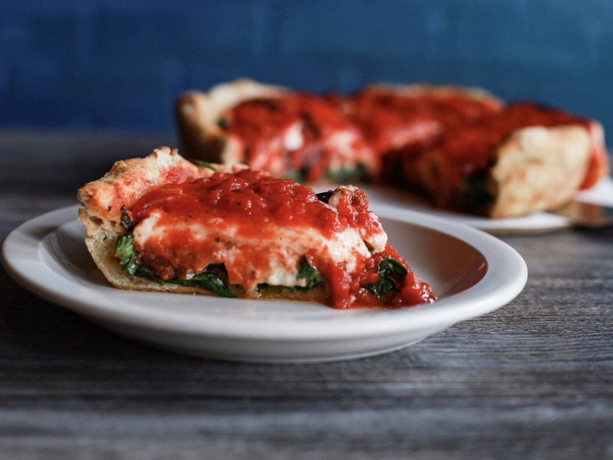 A thick slice of vegan deep-dish pizza sits on a small, round plate.