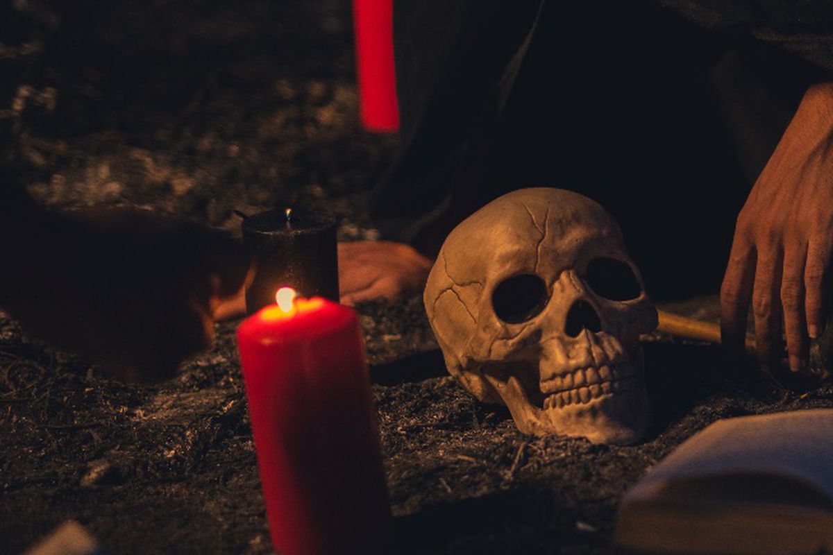 a skull head next to a hand with some red candles