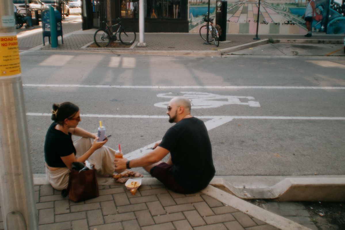 Two people sit and eat on a curb.