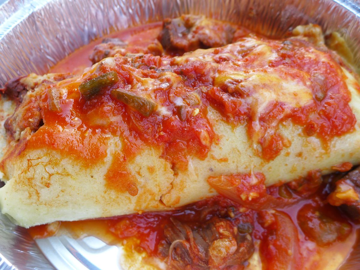 A thick burrito smothered in tomato sauce and pork chunks.
