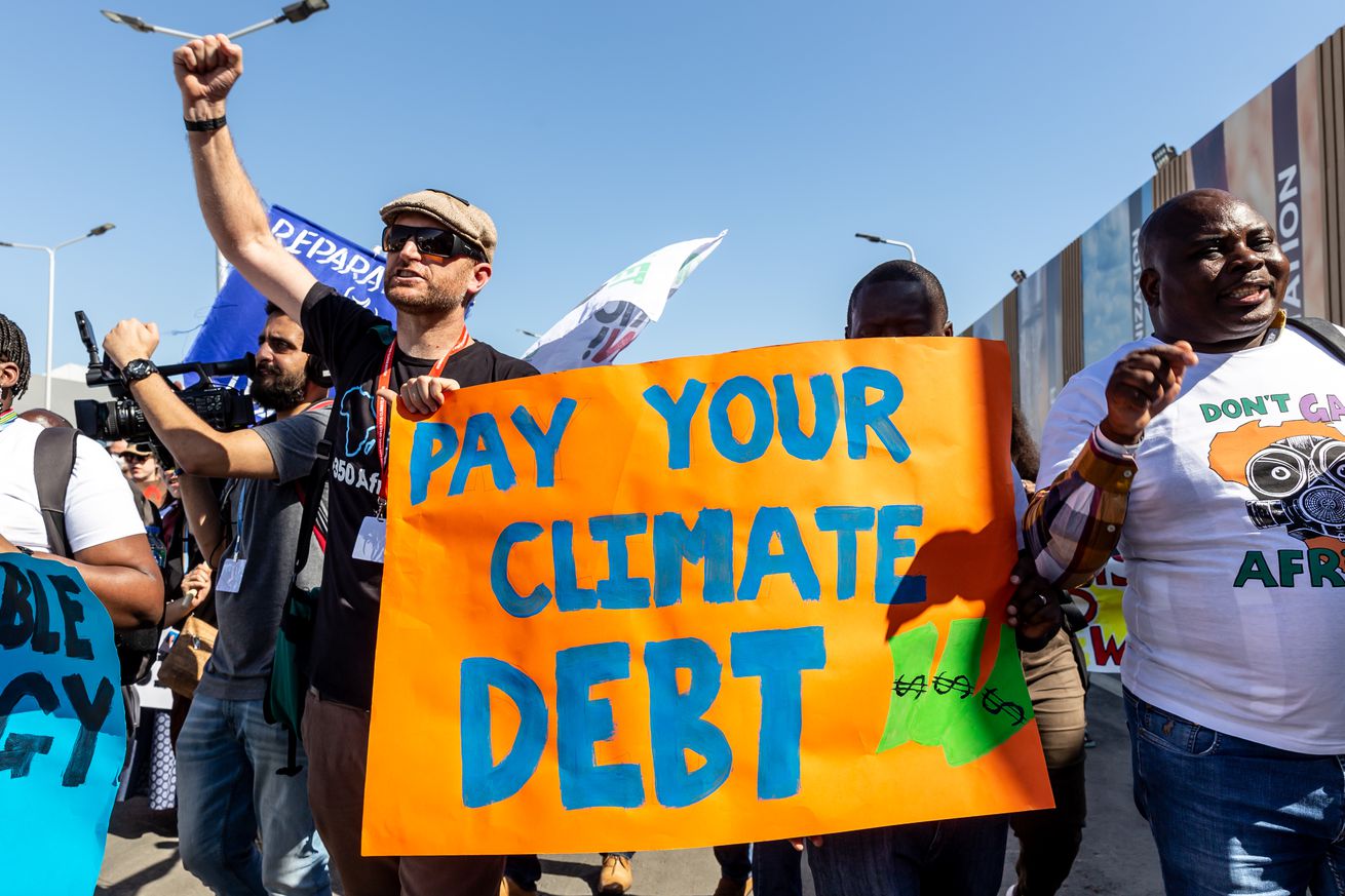 Protesters carry a sign that says “Pay your climate debt.”