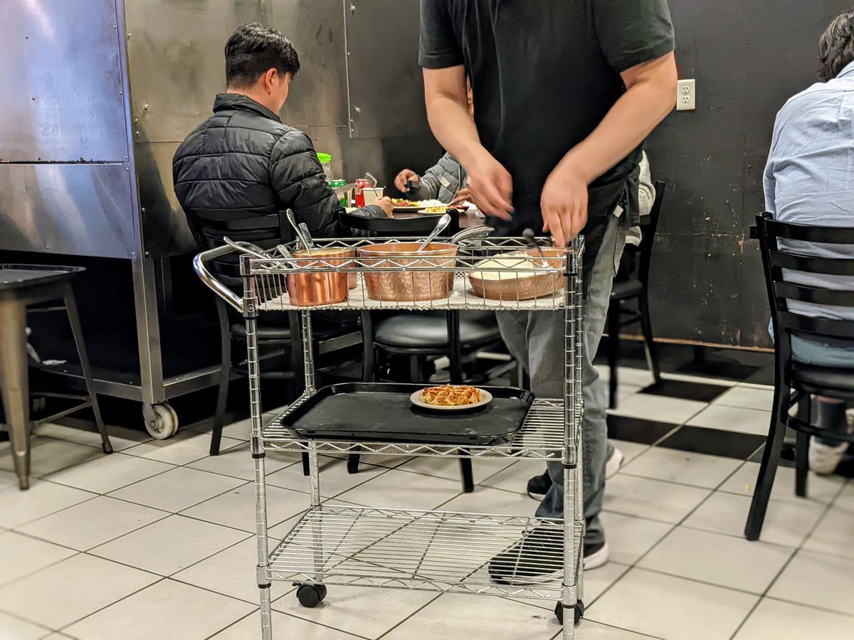 A server sets up dishes on a mobile tray inside of a  dining room.