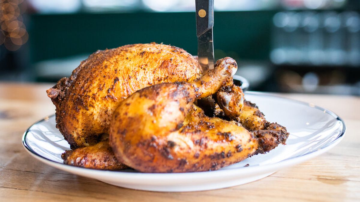 A knife stands upright, stuck into a whole rotisserie chicken on a restaurant table