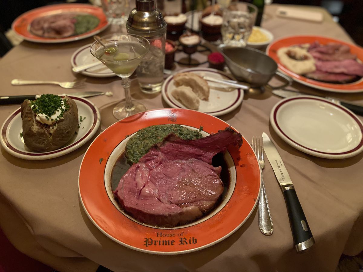 A thick slice of prime rib on a plate with creamed spinach, a baked potato, and a martini.