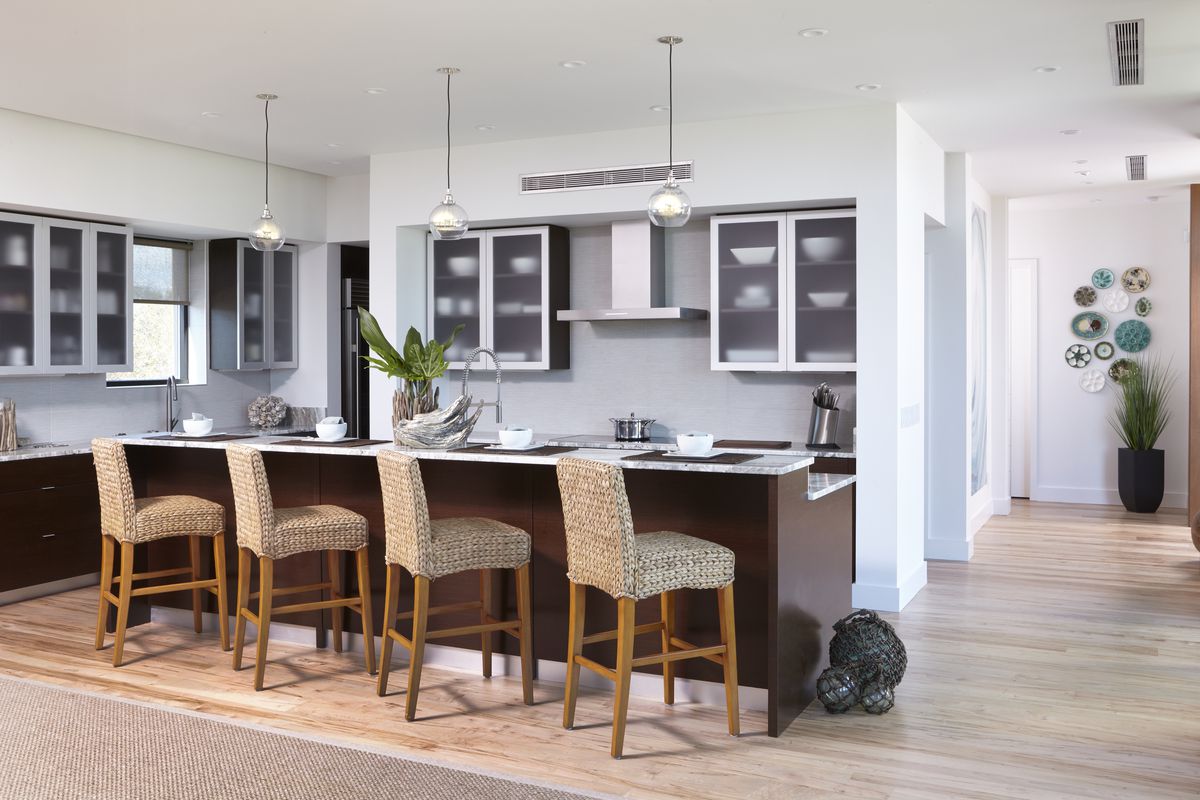 A modern kitchen with four barstools sitting at a large wooden island. 