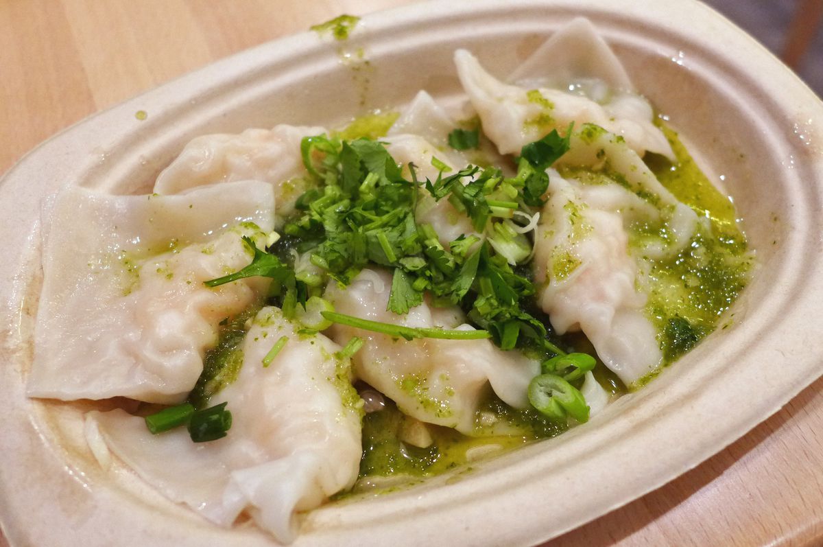 A bowl of dumplings with green herbs heaped on top. 
