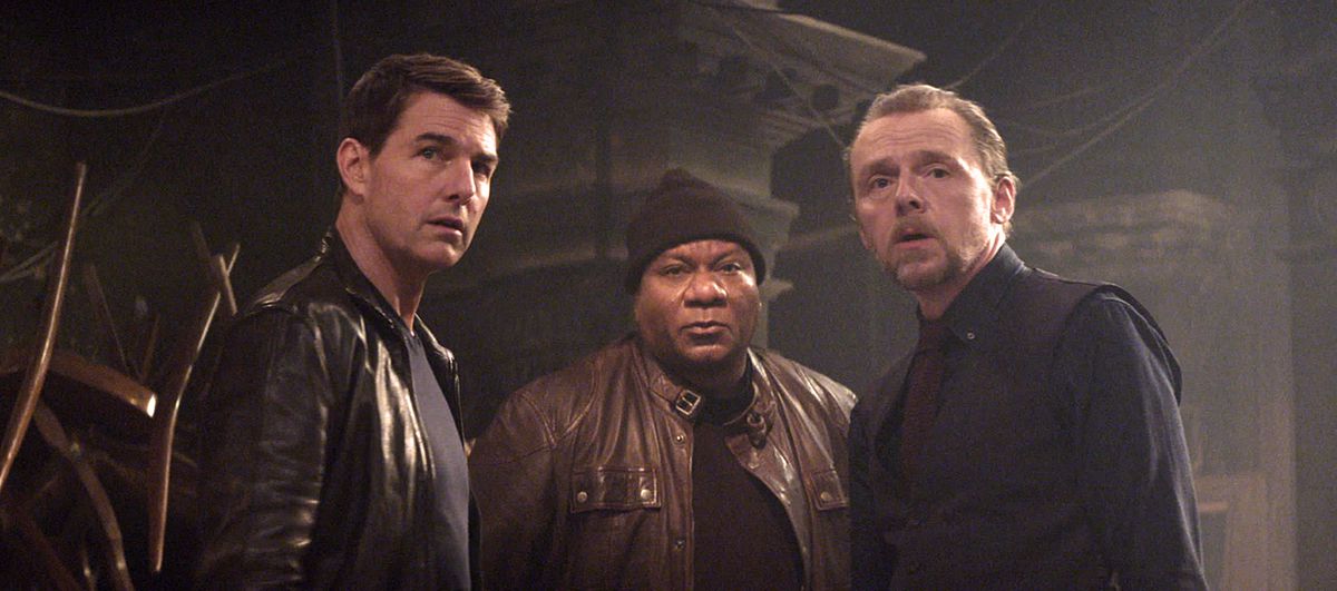 Ethan Hunt (Tom Cruise), Luther Stickell (Ving Rhames, in a black beanie and leather jacket) and Simon Pegg (in a black-on-black suit) stand in a semi-circle in Mission: Impossible Dead Reckoning Part One