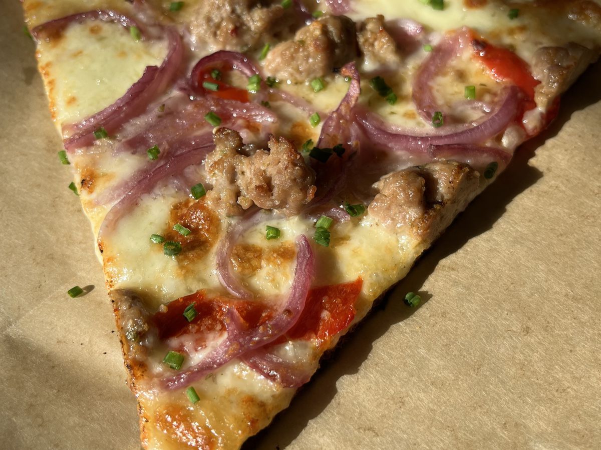 A slice of white pizza topped with onions and sausage.