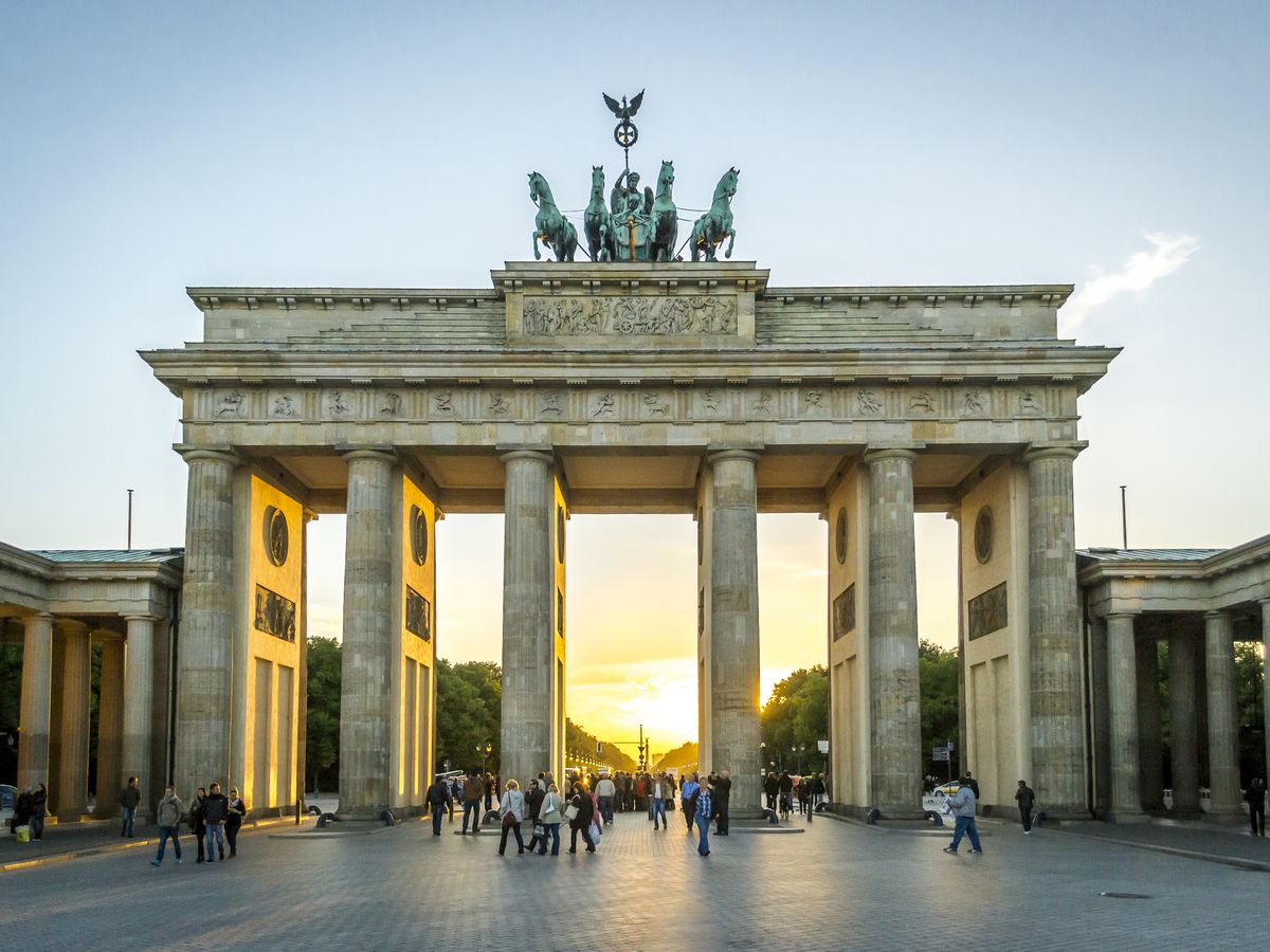 The exterior of the Brandenburg Gate in Berlin, Germany, at sunset. The gate has columns. There are statues on top of the gate. 