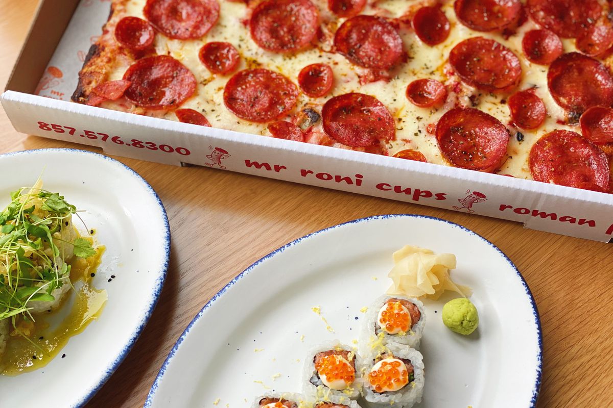 A salad, sushi roll, and pepperoni pizza situaded side by side on a wooden table 