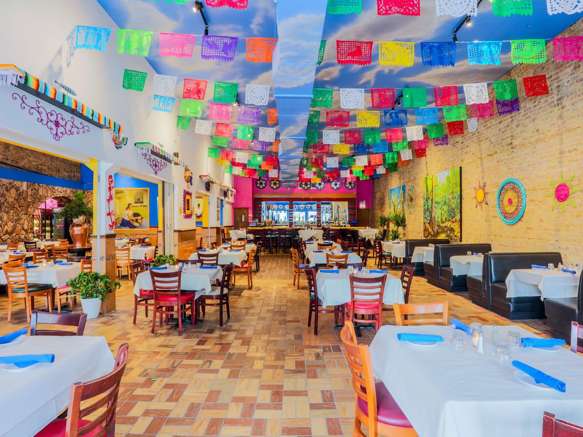 A large, long restaurant dining room decorated with colorful Mexican streamers.