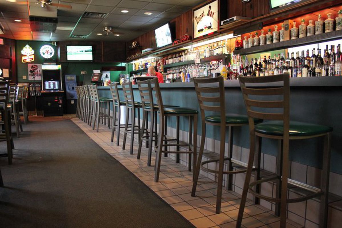 A line of stools before a green laminate bar. Behind the bar is a collection of booze bottles. 