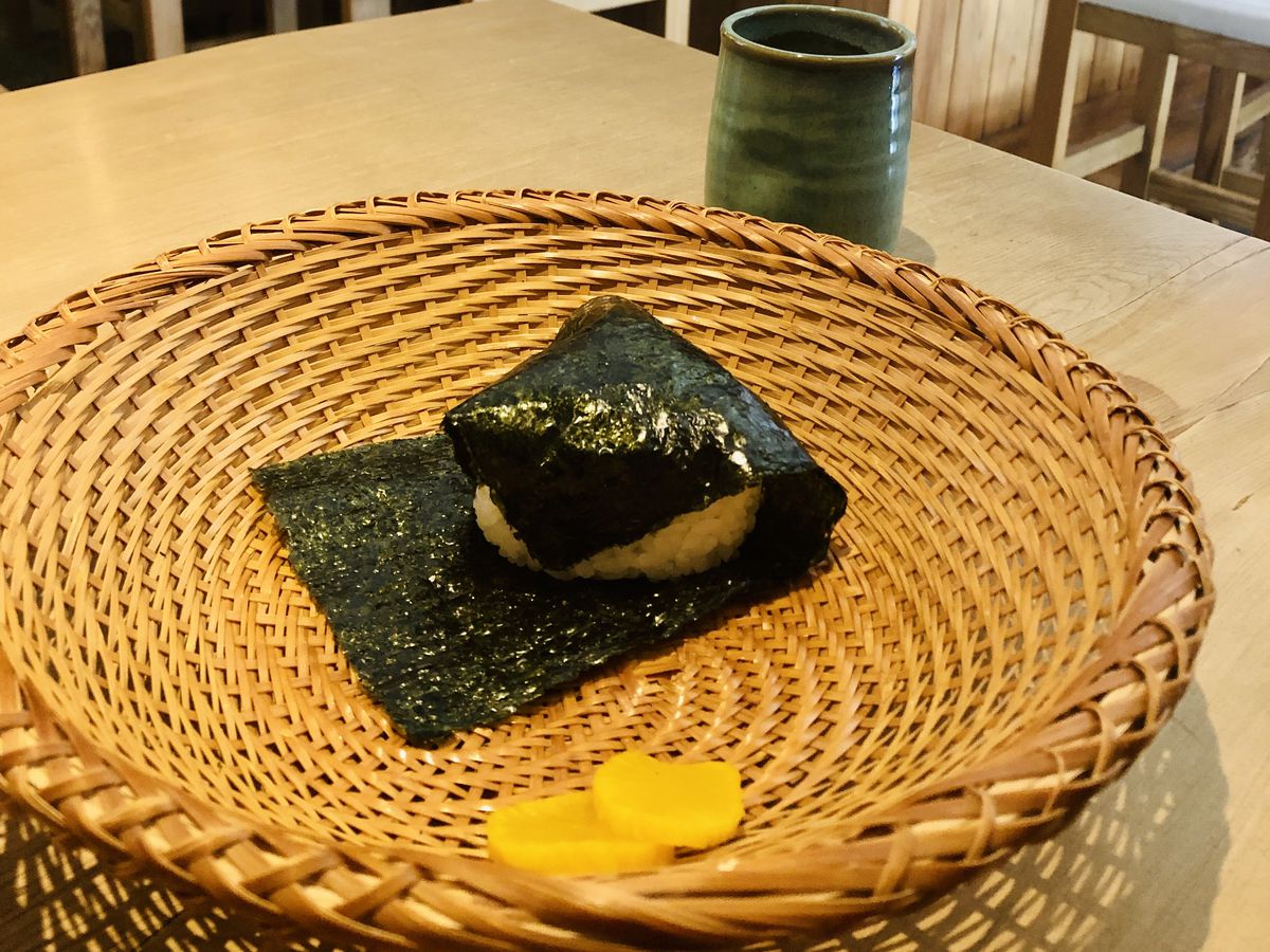 An onigiri presented in a woven bowl.