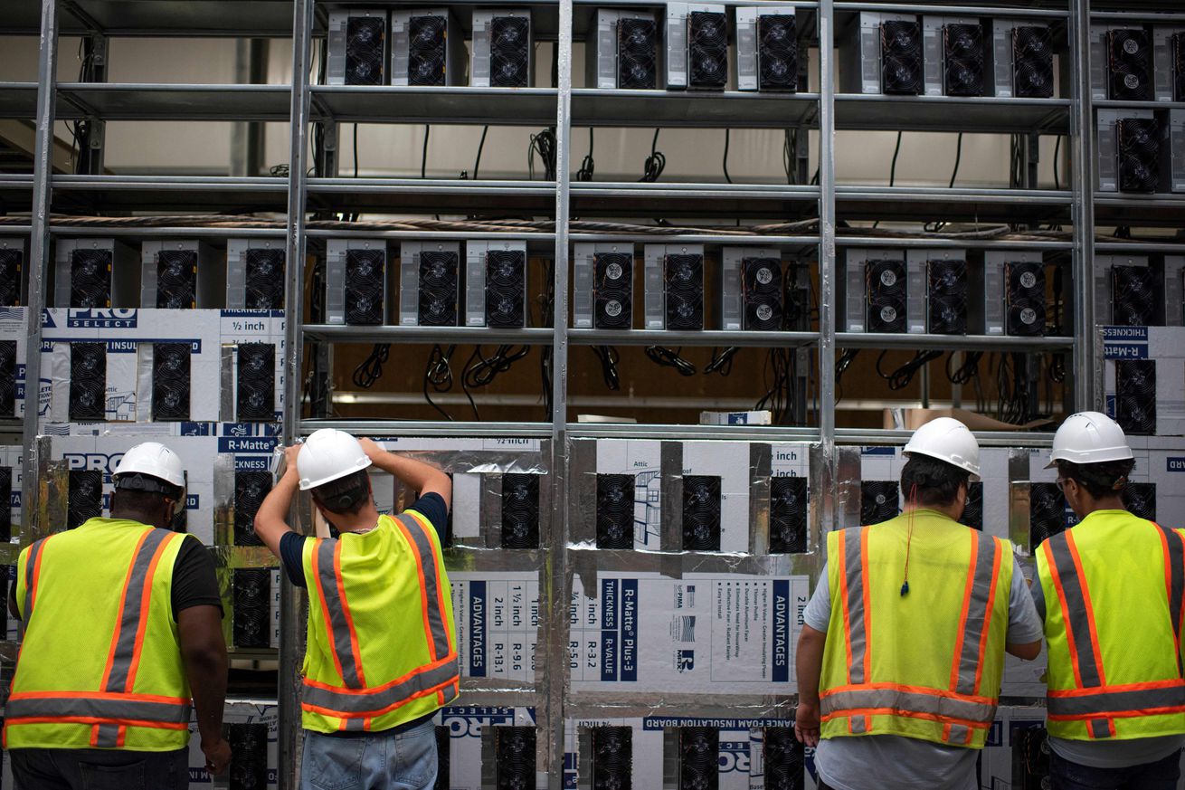 Workers install a new row of Bitcoin mining machines on a rack